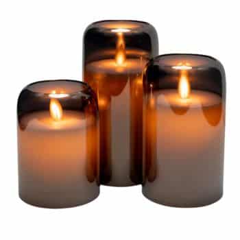 Three lit candles in cylindrical, smoky brown glass holders of varying heights, casting a warm, soft glow.
