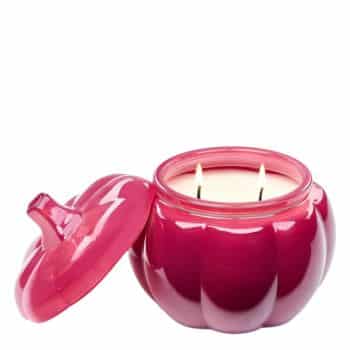 A pink, pumpkin-shaped candle jar with a matching lid set to the side, revealing a white two-wick candle inside.