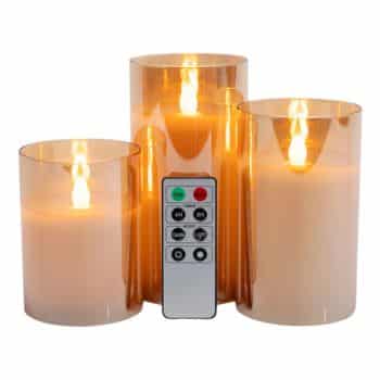 Three flameless LED candles of varying heights glow warmly, grouped together with a remote control placed in front of them for easy operation.