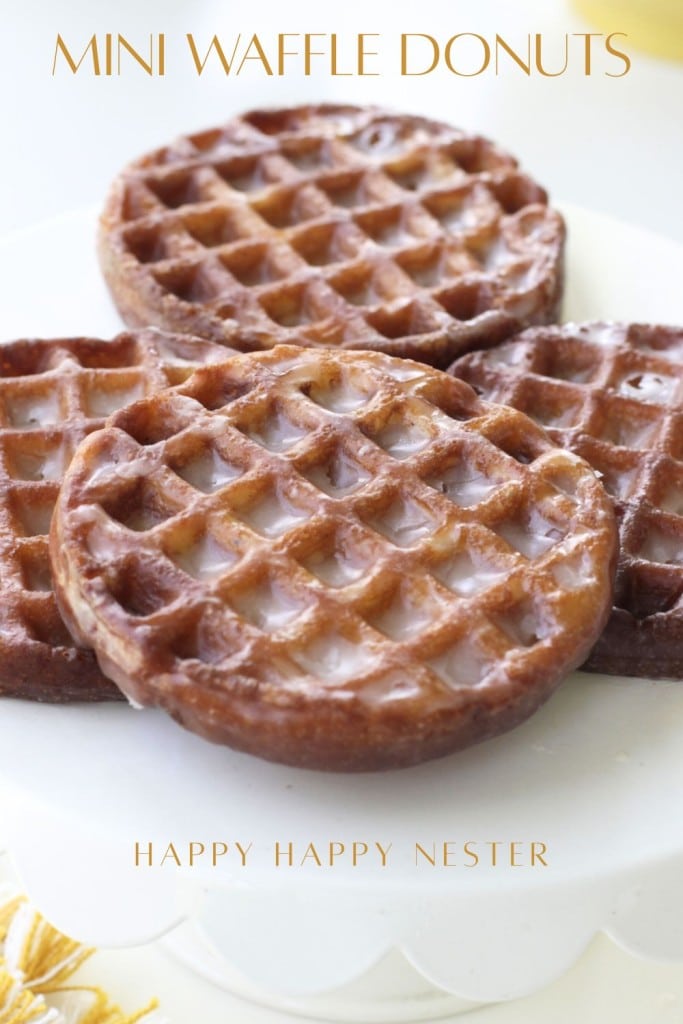 Three mini waffle donuts with a shiny glaze are stacked on a white plate. The text "MINI WAFFLE DONUTS" appears at the top, highlighting this delightful mini waffle donuts recipe from "HAPPY HAPPY NESTER.