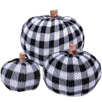 Three decorative pumpkins with black and white buffalo plaid knit covers and short brown stems, arranged together in varying sizes against a white background.