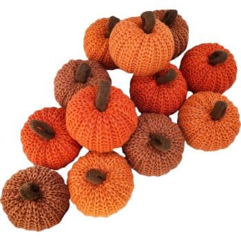 A group of small, knitted pumpkins in various shades of orange and brown, each with a protruding brown stem, arranged in a casual pile.