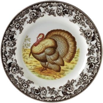 A decorative plate featuring a detailed turkey illustration in the center, surrounded by an ornate floral black and white border—perfect for serving my favorite Thanksgiving recipes against a grassy landscape backdrop.