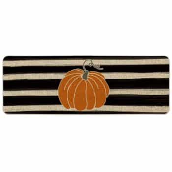 A rectangular rug with black and beige horizontal stripes features an orange pumpkin with a curling stem in the center.