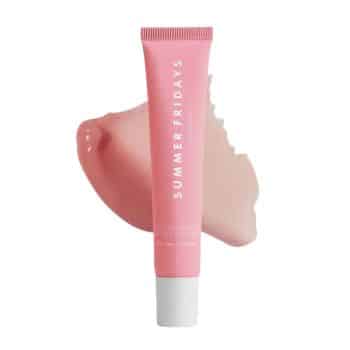 A pink tube of Summer Fridays lip balm stands upright in front of a smear of light pink balm, against a white background.
