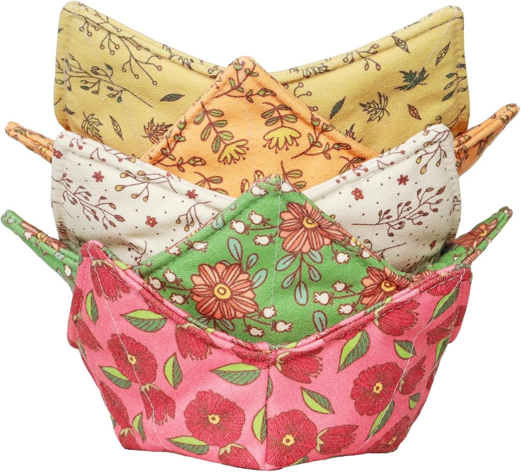 Four fabric bowl cozies are stacked together, each displaying a different floral or leaf print in pink, green, cream, and yellow. Perfect for serving my favorite Thanksgiving recipes, these quilted bowls protect hands from hot dishes.