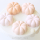 Five pastel pumpkin-shaped desserts sit on a round white cake stand, arranged in a circle. These chocolate pumpkins, in soft shades of pink and peach, create a delicate and elegant Halloween recipe presentation.