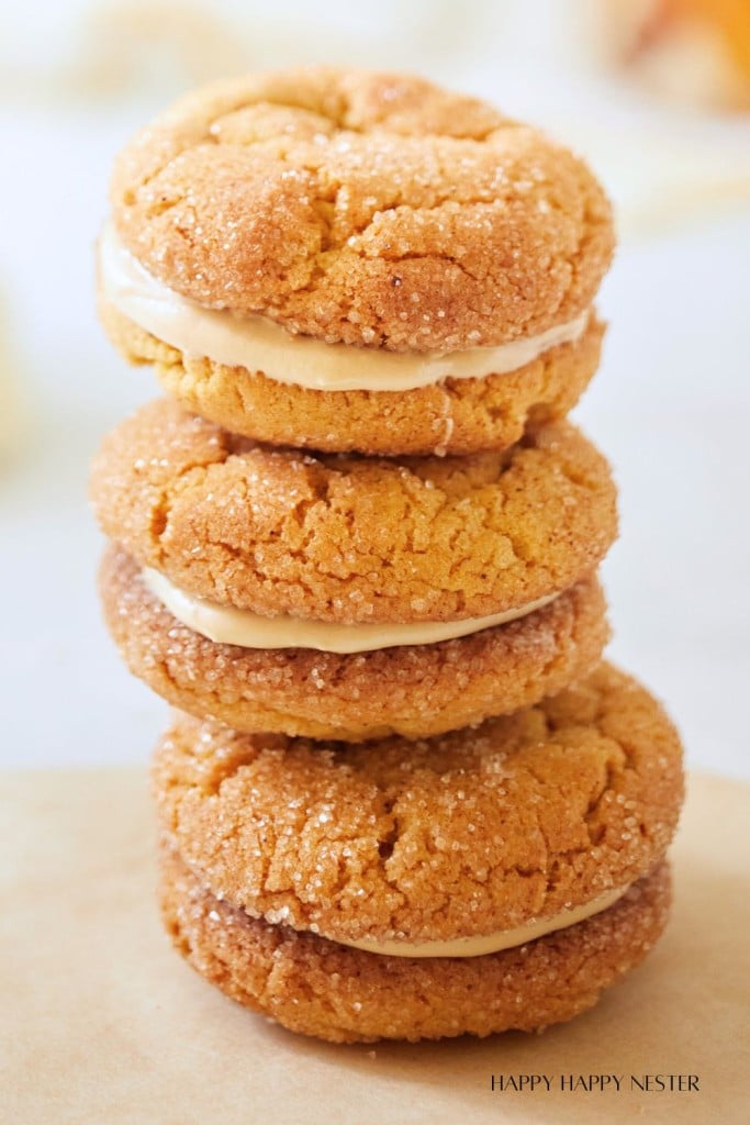A stack of three sandwich cookies with a creamy filling, inspired by all things pumpkin, coated in sugar and displayed on a light surface.