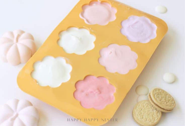 A yellow silicone mold with six flower-shaped sections filled with pastel-colored yogurt sits surrounded by cookies and meringue candies—perfect inspiration for your next Oreo Halloween treats recipe.