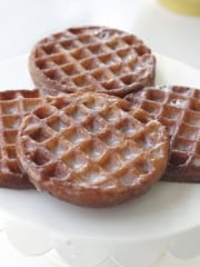 Three round glazed donuts and two rectangular glazed donuts with a waffle-like pattern are arranged on a white surface.