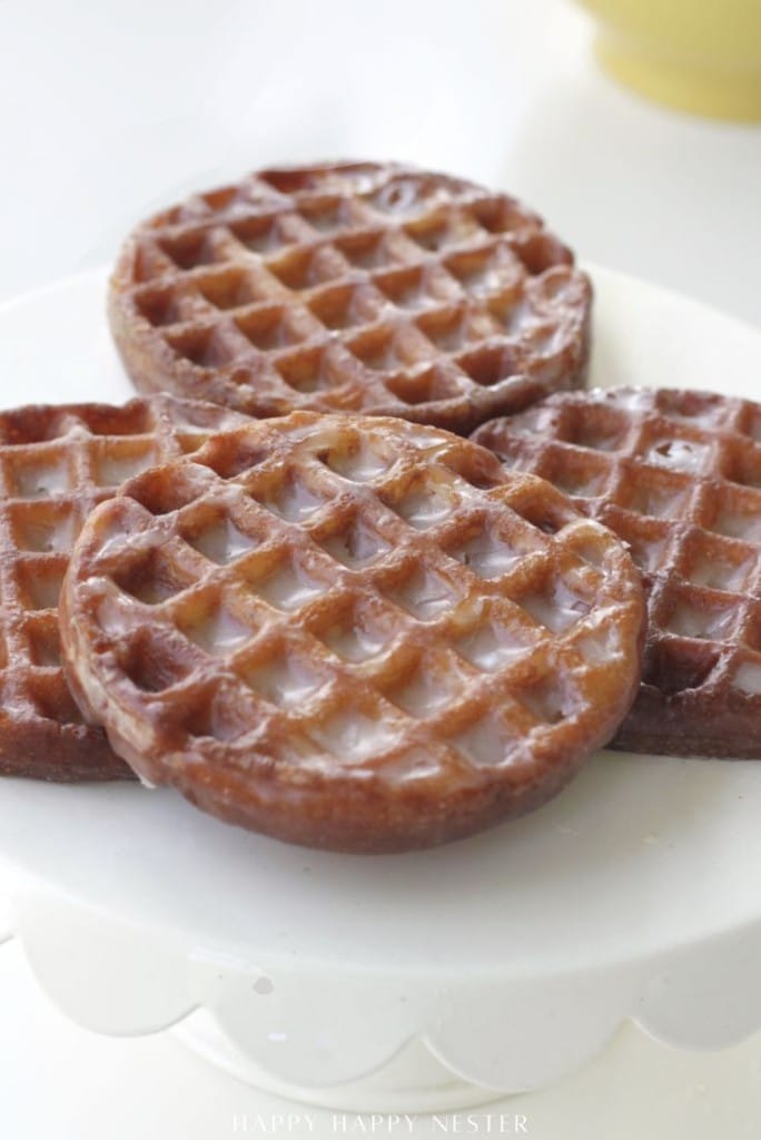 Three round glazed donuts and two rectangular glazed donuts with a waffle-like pattern are arranged on a white surface.