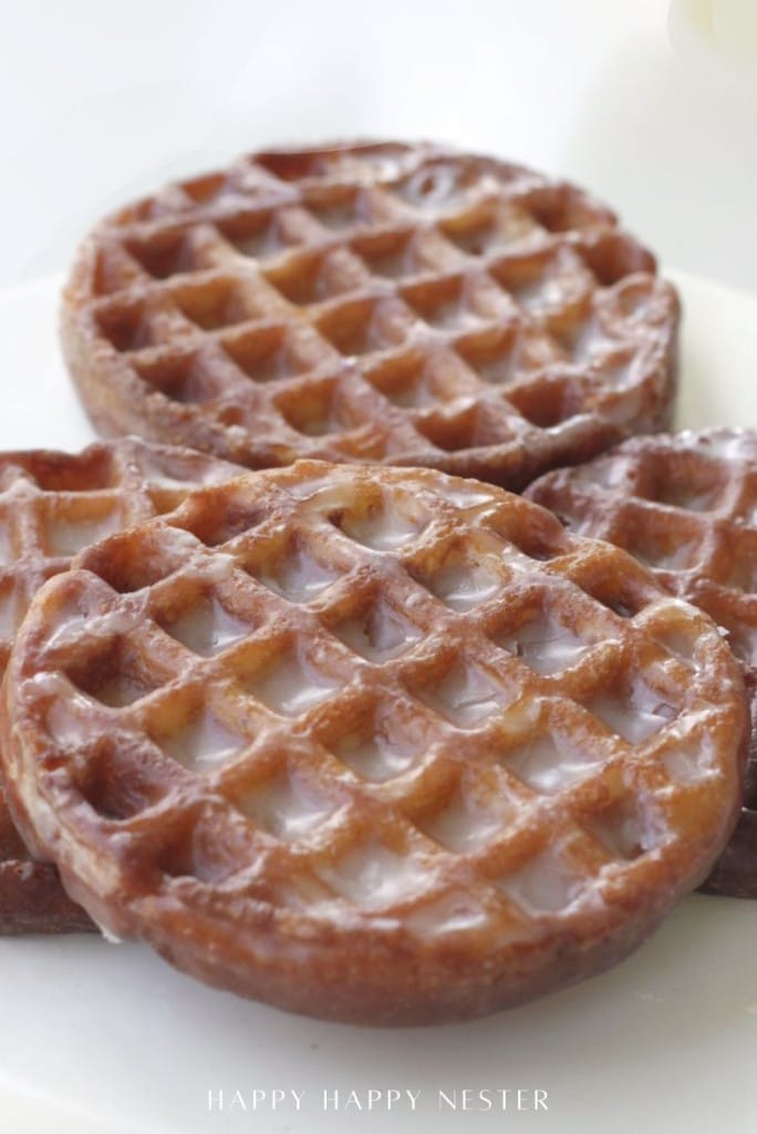 Three round glazed pastries with a waffle pattern are stacked on a white plate. The light glaze gives them a shiny appearance—an irresistible treat inspired by our mini waffle donuts recipe.