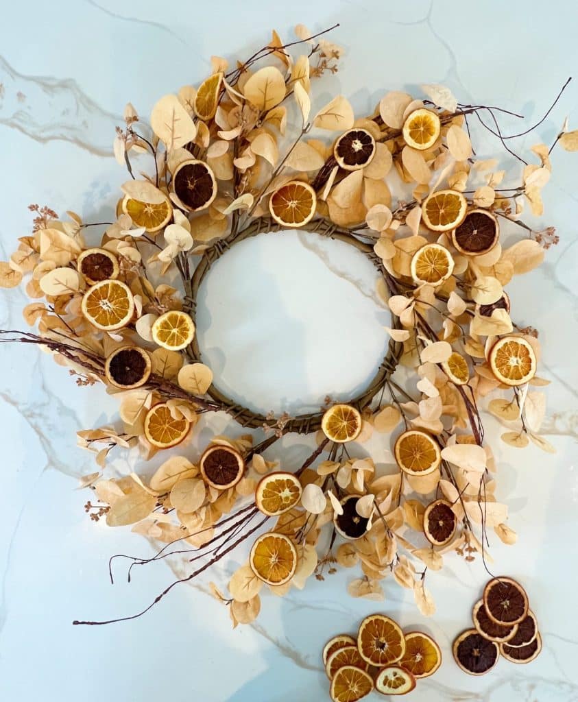 A decorative wreath made of dried orange slices, cream-colored leaves, and twigs arranged in a circle on a light, marble-patterned surface—perfect wall crafts for fall, with extra dried orange slices scattered nearby for a cozy touch.