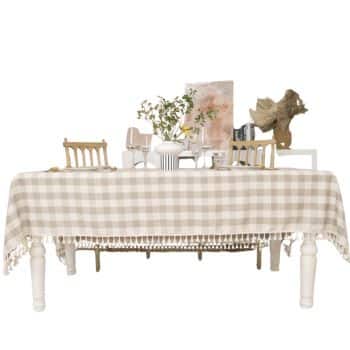 A dining table with a beige and white checkered tablecloth, topped with my favorite Thanksgiving decor—dishes, glasses, a small vase with green branches, books, and unique art pieces for a festive touch.