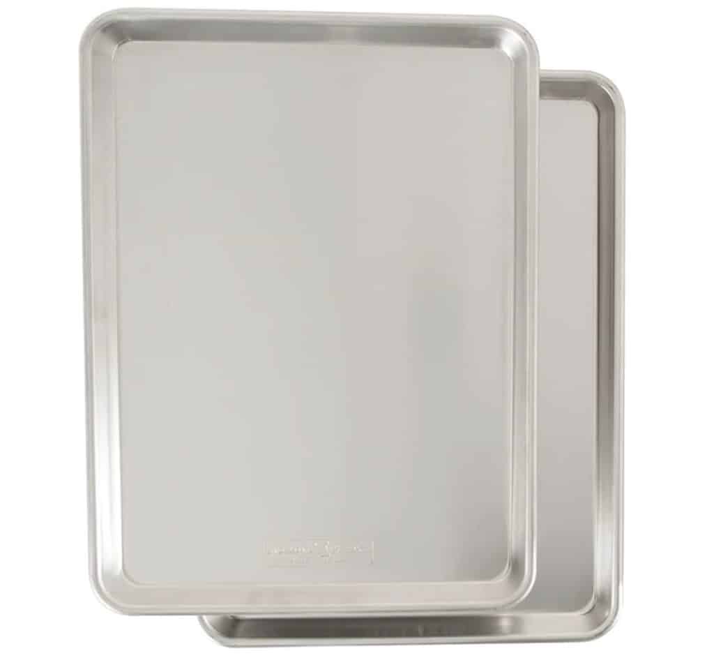 Two shiny, silver aluminum baking sheets stacked slightly askew, with smooth surfaces and raised edges, perfect for preparing your favorite Halloween bark recipe, on a white background.