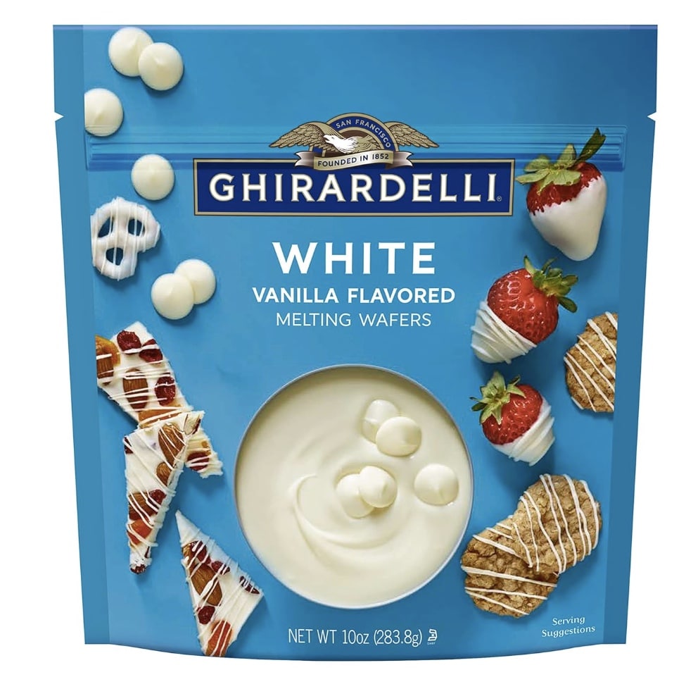 A blue bag of Ghirardelli White Vanilla Flavored Melting Wafers, perfect for a Halloween bark recipe, featuring images of strawberries, cookies, and pretzels coated in white chocolate, with the wafers shown in a bowl on the front.