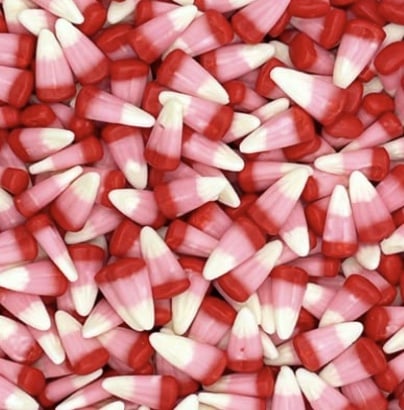 A pile of pink, red, and white candy corn pieces, with most featuring a red base, a pink middle, and a white tip—perfect for topping your favorite Halloween bark recipe.