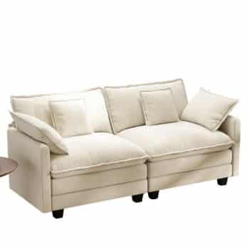 A cream-colored, modern sofa with four large seat cushions, five matching back pillows, and two side pillows. The sofa has short black legs and is placed on a white background.