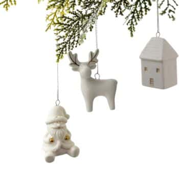 Three white Christmas ornaments—a Santa, a reindeer, and a house—hang from a branch with green foliage at the top. The background is white, making the ornaments stand out clearly.
