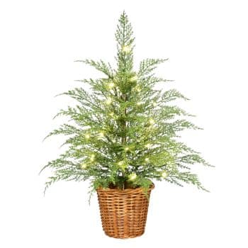 Small artificial Christmas tree with green branches, decorated with white string lights, placed in a woven brown basket.