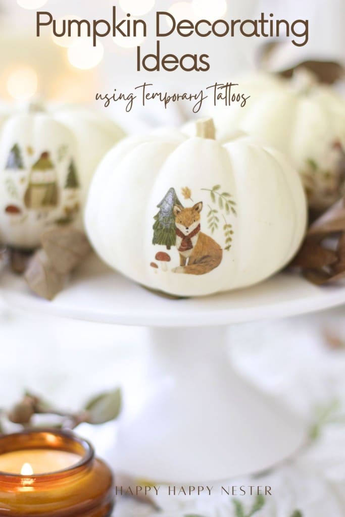 White pumpkins decorated with woodland animal and nature-themed temporary tattoos sit on a white cake stand. Text at the top reads, "Pumpkin Decorating Ideas Without Carving Using Temporary Tattoos." A lit candle glows in the foreground.