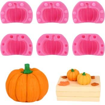 Six pink silicone pumpkin molds are displayed above a large orange pumpkin and two smaller pumpkins on a rectangular base, possibly a cake or block, with decorative leaves—perfect for crafting festive Thanksgiving treats.