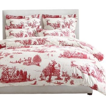 A neatly made bed with white bedding featuring a red toile de Jouy pattern, including scenic countryside images, and matching pillows arranged against a white headboard.