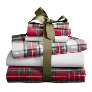 A stack of folded plaid and white bed sheets tied together with an olive green ribbon bow, resembling a neatly wrapped gift.