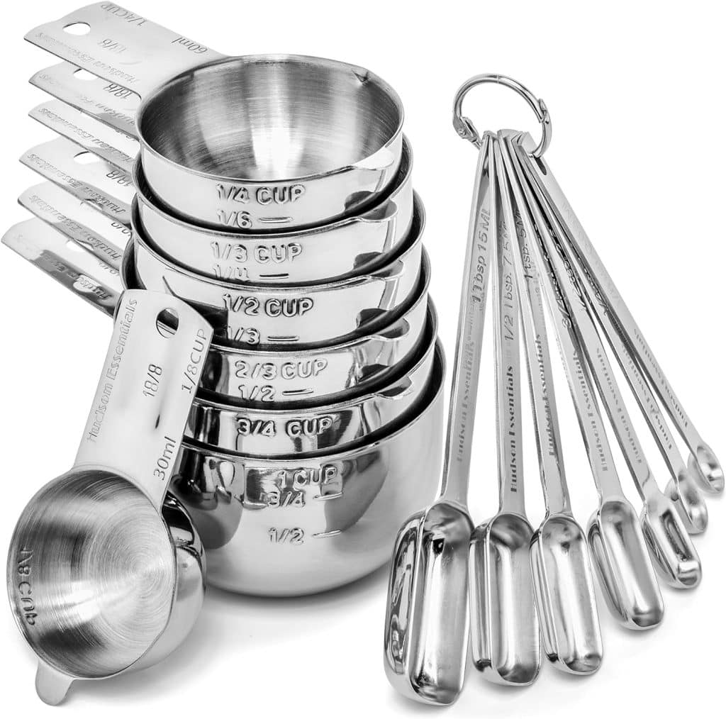 A set of stainless steel measuring cups and spoons, neatly stacked and arranged, perfect for following your favorite pumpkin bread pudding recipe. Each shiny piece displays engraved measurements, reflecting light beautifully.