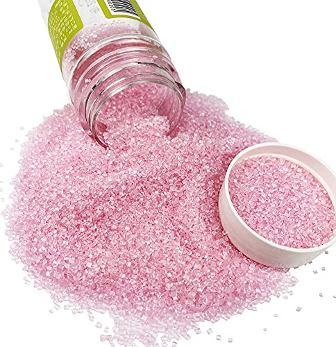 A clear plastic jar tipped over, spilling pink decorative sugar crystals onto a white surface—perfect for topping your favorite Halloween bark recipe. The white lid rests next to the sparkling pile of sugar.