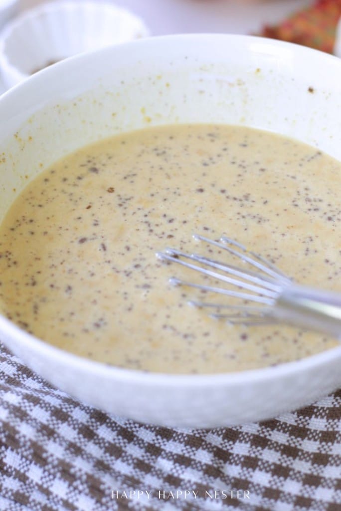 A large white bowl filled with a creamy, speckled pumpkin bread pudding recipe batter and a metal whisk, resting on a checkered cloth.