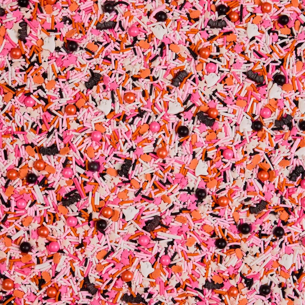 A close-up of colorful sprinkles, featuring pink, orange, white, and black shapes—perfect for topping your favorite Halloween bark recipe—scattered densely to create a festive and vibrant pattern.