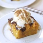 A slice of pumpkin bread pudding recipe topped with vanilla ice cream and a sprinkle of cinnamon, served on a white plate with a checkered napkin underneath.