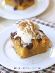 A slice of pumpkin bread pudding recipe topped with vanilla ice cream and a sprinkle of cinnamon, served on a white plate with a checkered napkin underneath.