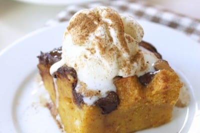 A slice of pumpkin bread pudding recipe topped with vanilla ice cream and a sprinkle of cinnamon, served on a white plate with a checkered napkin underneath.