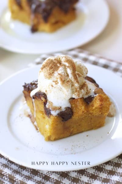 A slice of pumpkin bread pudding recipe topped with vanilla ice cream and a sprinkle of cinnamon, served on a white plate with a checkered napkin underneath.