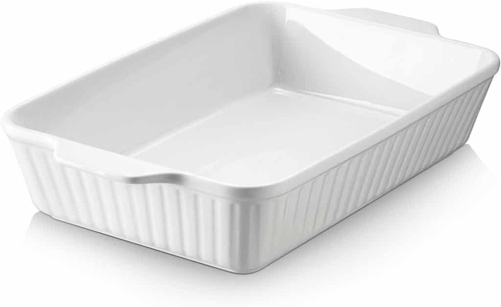A white rectangular ceramic baking dish with slightly flared sides and ribbed exterior, perfect for showcasing your favorite pumpkin bread pudding recipe, is placed on a white surface.