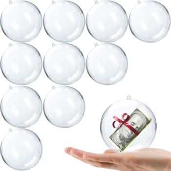 A hand holds a clear ornament filled with a rolled dollar bill tied with a red ribbon—a festive idea for Christmas tree crafts. Around it, eleven empty, clear ornaments are neatly arranged in rows.