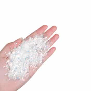 A hand holds a small pile of clear and iridescent plastic flakes against a white background, perfect for adding sparkle to my favorite holiday home crafts.