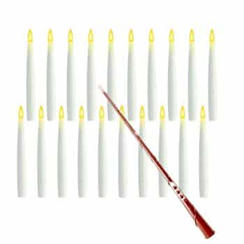 A set of sixteen white flameless LED taper candles with yellow tips, arranged in rows. A brown remote control wand for turning the candles on and off is placed diagonally across the bottom.