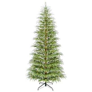 A tall, artificial Christmas tree with green branches lightly dusted with white, resembling snow, standing on a black metal stand against a white background.