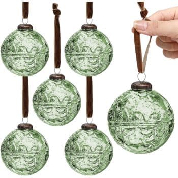 Six green, textured glass Christmas ornaments with brown ribbons are shown hanging. One ornament is being held by a hand in the upper right corner.