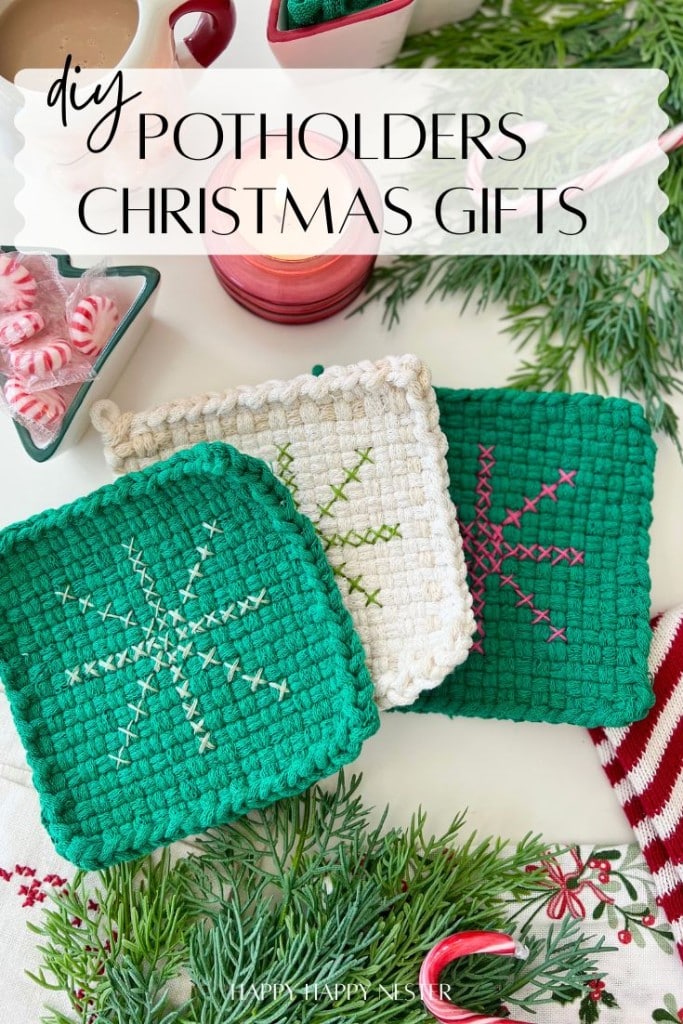 Three handmade potholders—two green and one white—with stitched snowflake designs rest on a table adorned with pine branches, candy canes, and a mug, making charming DIY Christmas gifts that evoke a festive holiday atmosphere.