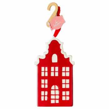 A red and white Christmas ornament shaped like a tall, narrow house with multiple windows and a decorative roof, hanging by a gold hook with a pink tag.