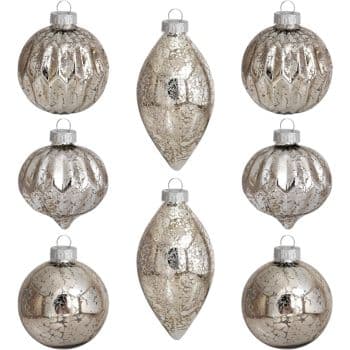 Nine vintage-style silver Christmas ornaments in three different shapes: round, elongated teardrop, and ribbed. They have a mottled, antique finish and are arranged in a grid pattern against a white background.
