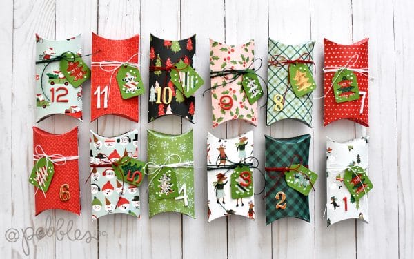 Twelve colorful, decorated pillow boxes numbered 1 to 12, each tied with string and a holiday gift tag, arranged in rows on a white wooden surface—one of my favorite holiday home crafts, perfect as a festive Christmas advent calendar.