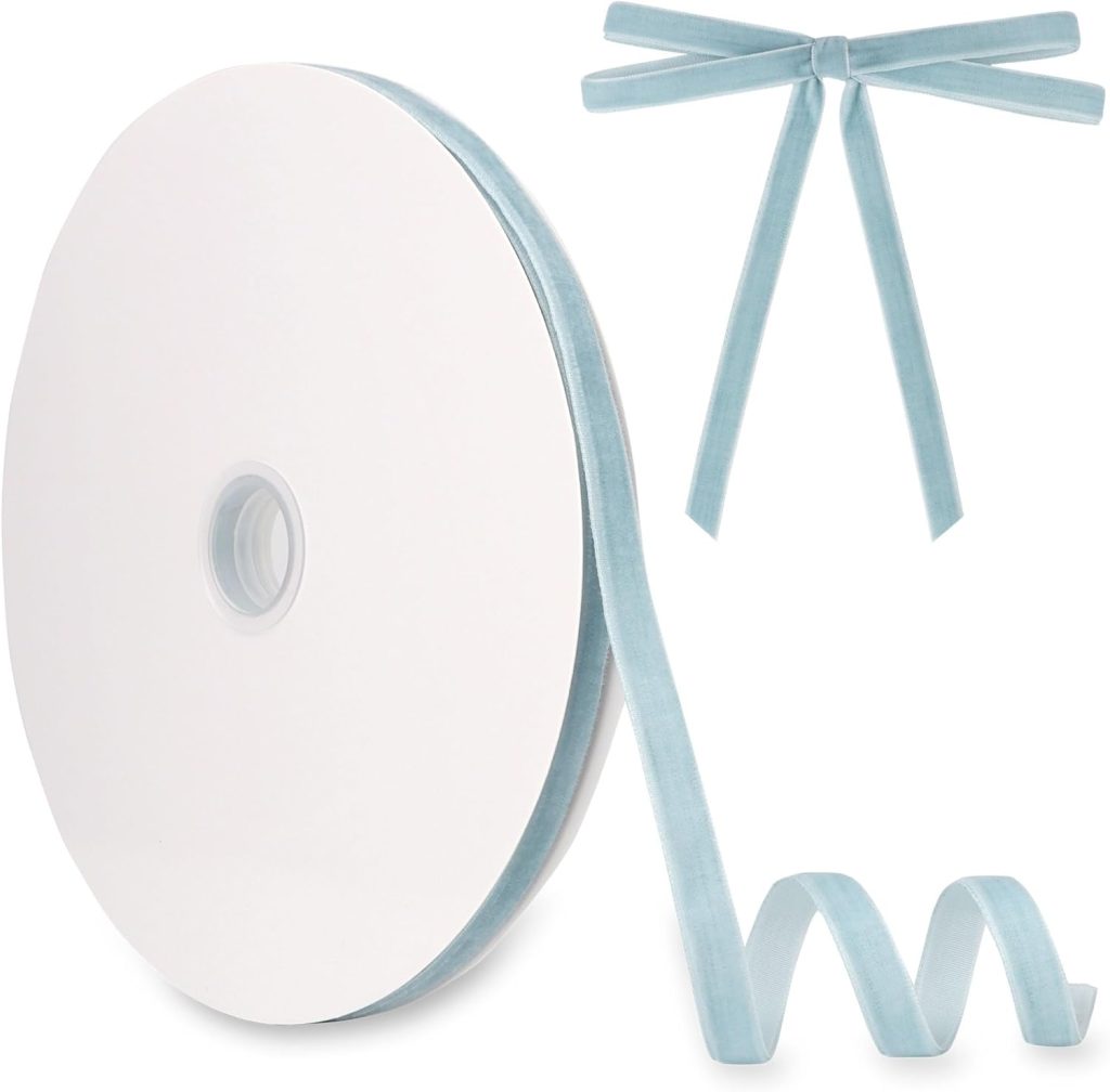A spool of light blue velvet ribbon with part unwound and curled, perfect for DIY Christmas ornaments. A separate bow made from the same ribbon is displayed in the upper right corner, adding a charming vintage style touch.