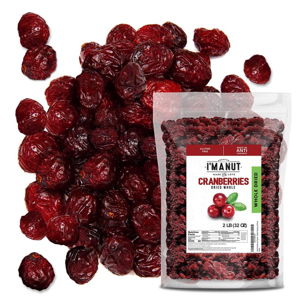 A clear plastic bag labeled “Manut Cranberries Dried Whole” sits on a pile of dried whole cranberries—perfect for simmer pot recipes or festive gifts. The 2-pound bag shows cranberries inside, with some scattered outside.