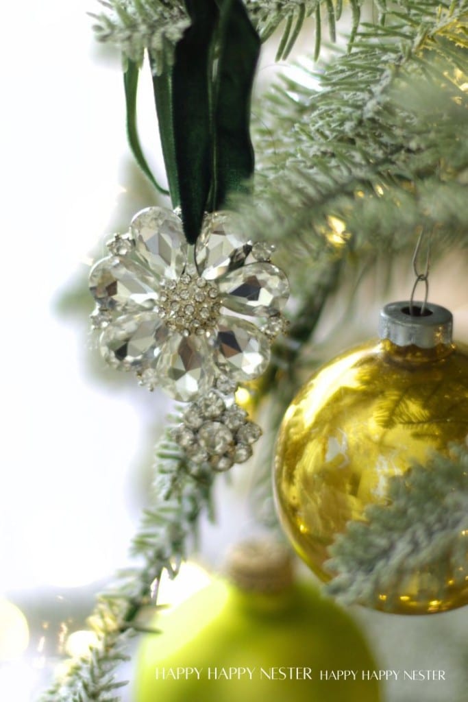 A close-up of a sparkling crystal snowflake ornament and a shiny yellow bauble, capturing the charm of vintage style Christmas ornaments DIY, hanging on a frosted Christmas tree branch.