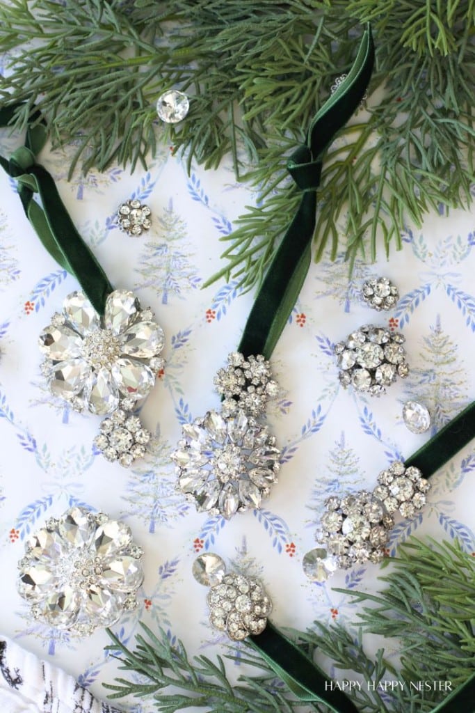 Vintage rhinestone brooches and earrings are arranged on festive patterned paper with green velvet ribbons and pine branches, evoking a sparkling holiday theme.